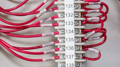 Serie di fili rossi all’interno di una morsettiera identificata da un’etichetta bianca.