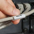 Persona che tiene in mano un’etichetta wrap around applicata a un cavo grigio.