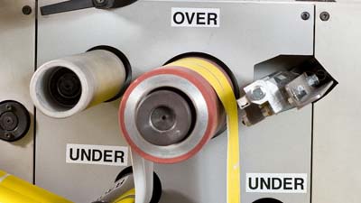 Varie etichette in vinile ognitempo Brady con testo OVER e UNDER, applicate su una macchina fustellatrice per indicare la direzione secondo cui infilare il materiale.