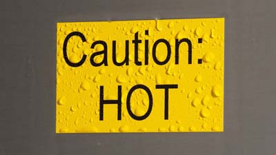 Etichetta ToughWash Brady gialla con testo CAUTION HOT stampato. L’etichetta è bagnata come se fosse stata pulita di recente con uno spray.