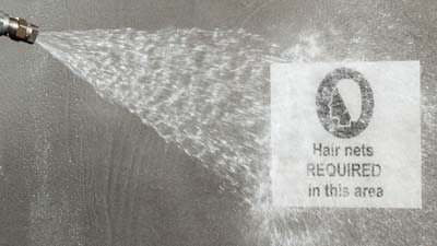 Operatore che utilizza un getto d’acqua per pulire un’etichetta rilevabile al metal detector ToughWash Brady applicata su un macchinario.