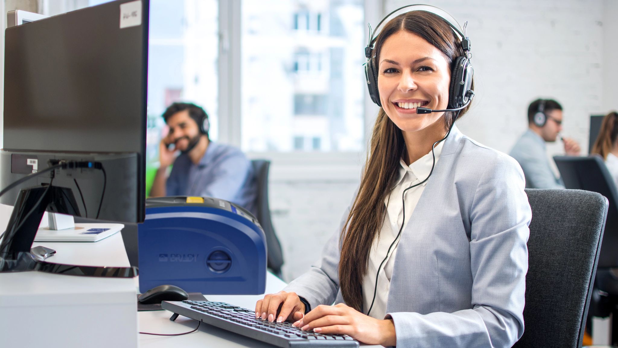 Persona che tiene in mano un telefono. Lo schermo del telefono mostra un’etichetta gialla brillante creata con Express Labels Mobile. Sullo sfondo una vaschetta di plastica con l’etichetta reale stampata.